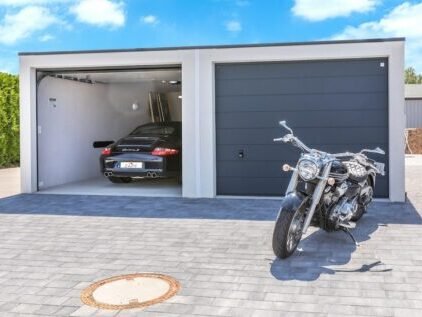 Garage individuelle avec une voiture garer à l'intérieur de celui-ci, la porte du garage est ouverte de façon a ce que le véhicule puisse entrer pour se garer. Une moto est stationné devant le garage.