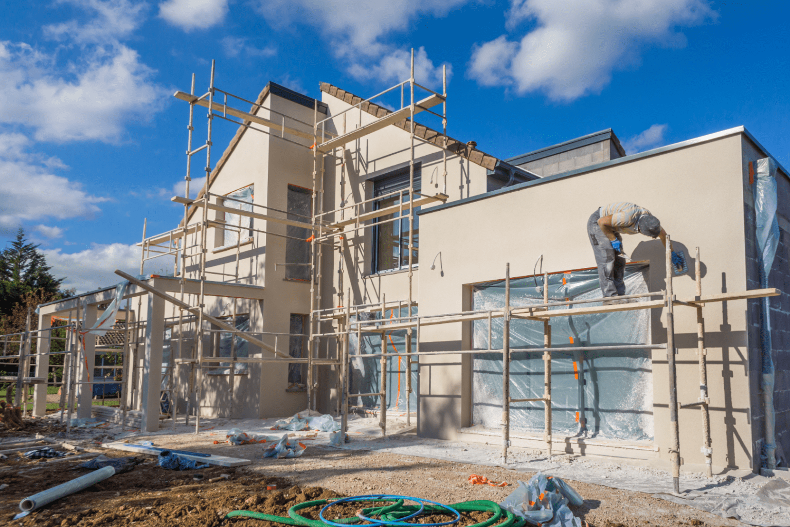 Chantier en cours, avec des maçons travaillant dans le chantier entrain d'achever la construction d'une maison. Il y à la présence d'échafaudage pour faire la façade de la maison